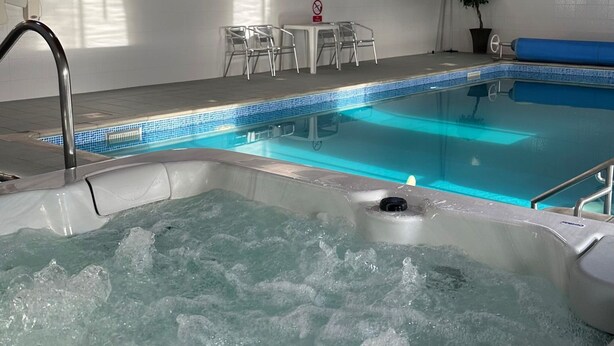 Ein Innenpool mit Whirlpool, Holzbalken und einer Sitzecke mit Sesseln.