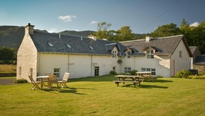 Ein Haus aus Stein mit einem geneigten Dach, einer Terrasse mit Tisch und Stühlen und Blick auf die umliegende Landschaft.
