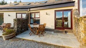 A house with a stone exterior, a tiled patio, and a wooden table with chairs.