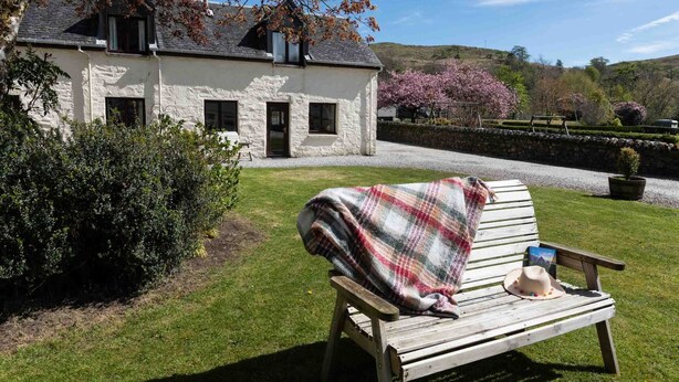 Una casa de piedra con un banco de jardín, un sombrero y un libro.
