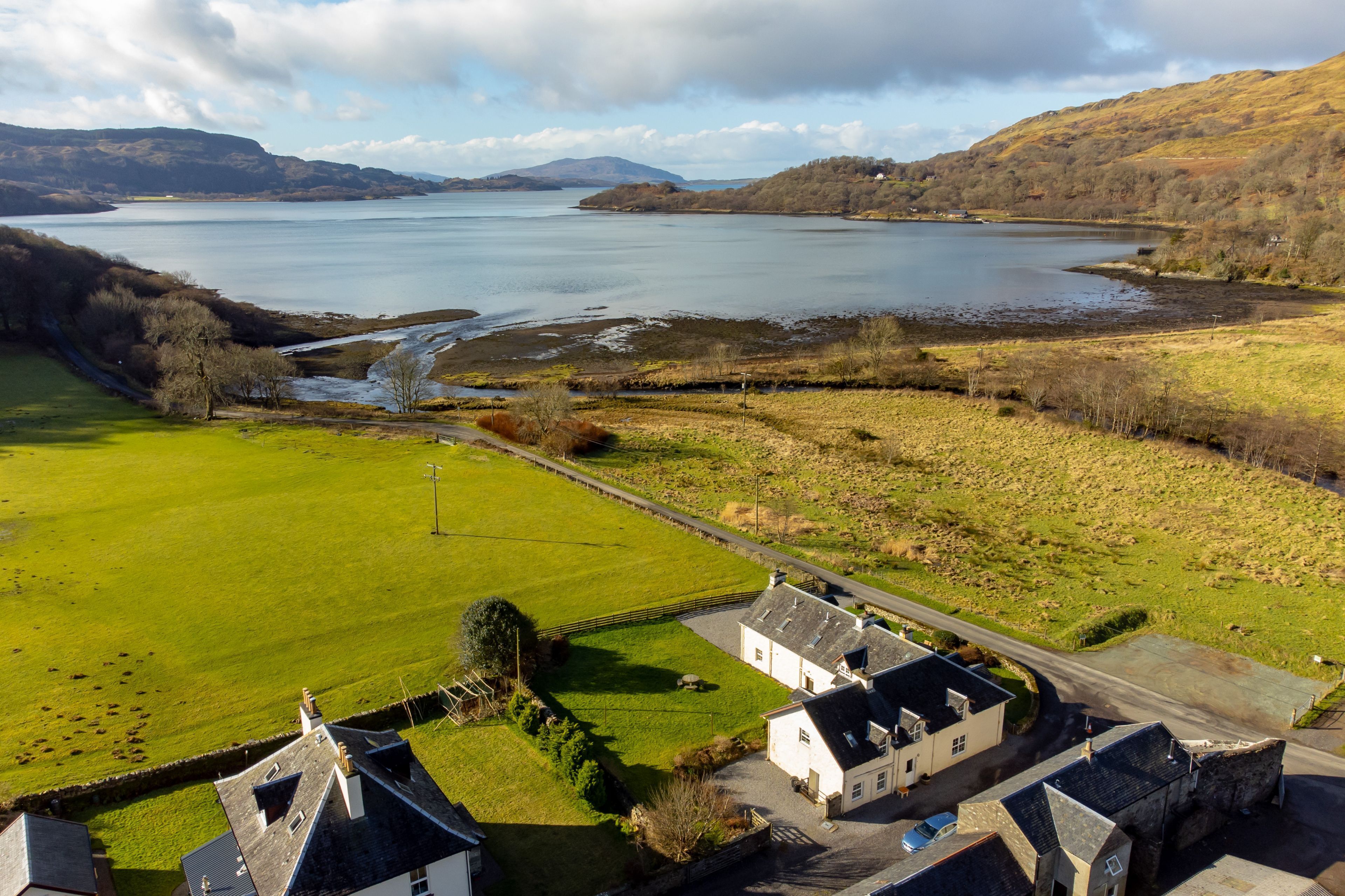 A rural landscape with a lake, green fields, and white buildings with grey roofs.