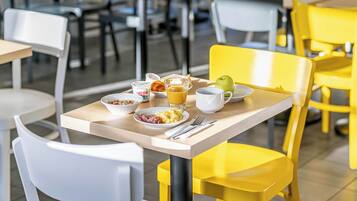 Un coin repas avec des chaises jaunes et blanches, une table où sont disposés des aliments pour le petit-déjeuner et un verre de jus d’orange.