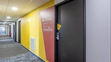 A hotel corridor with a yellow and red wall, a black door with a number, and a fire extinguisher.