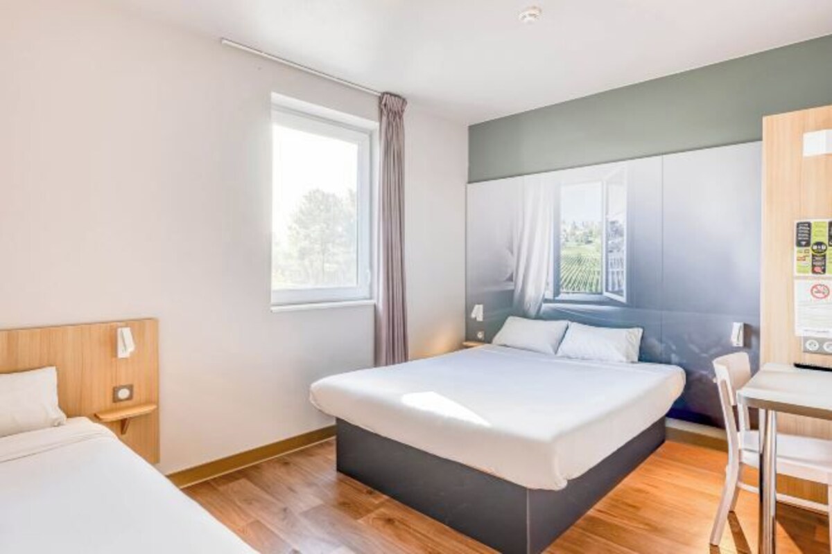 A modern hotel room with a large bed, a desk, and a window with curtains.