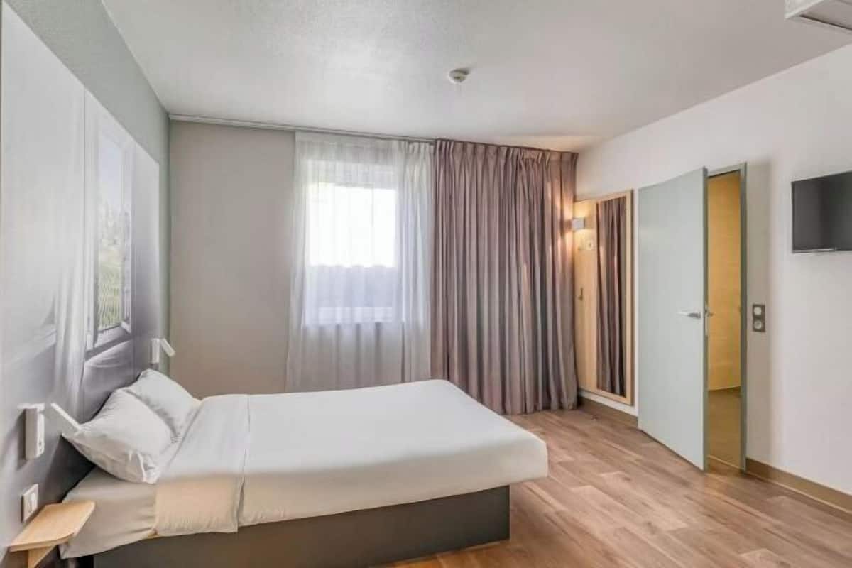 Een moderne hotelkamer met een bed, een televisie, een raam met gordijnen en een deur.