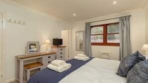 Un dormitorio con cama, mesitas de noche, televisor y ventana con cortinas.