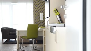 A modern kitchen with white cabinetry, a green chair, and a dining table. - ADAPT APARTMENT HOTEL Giessen (Giessen)