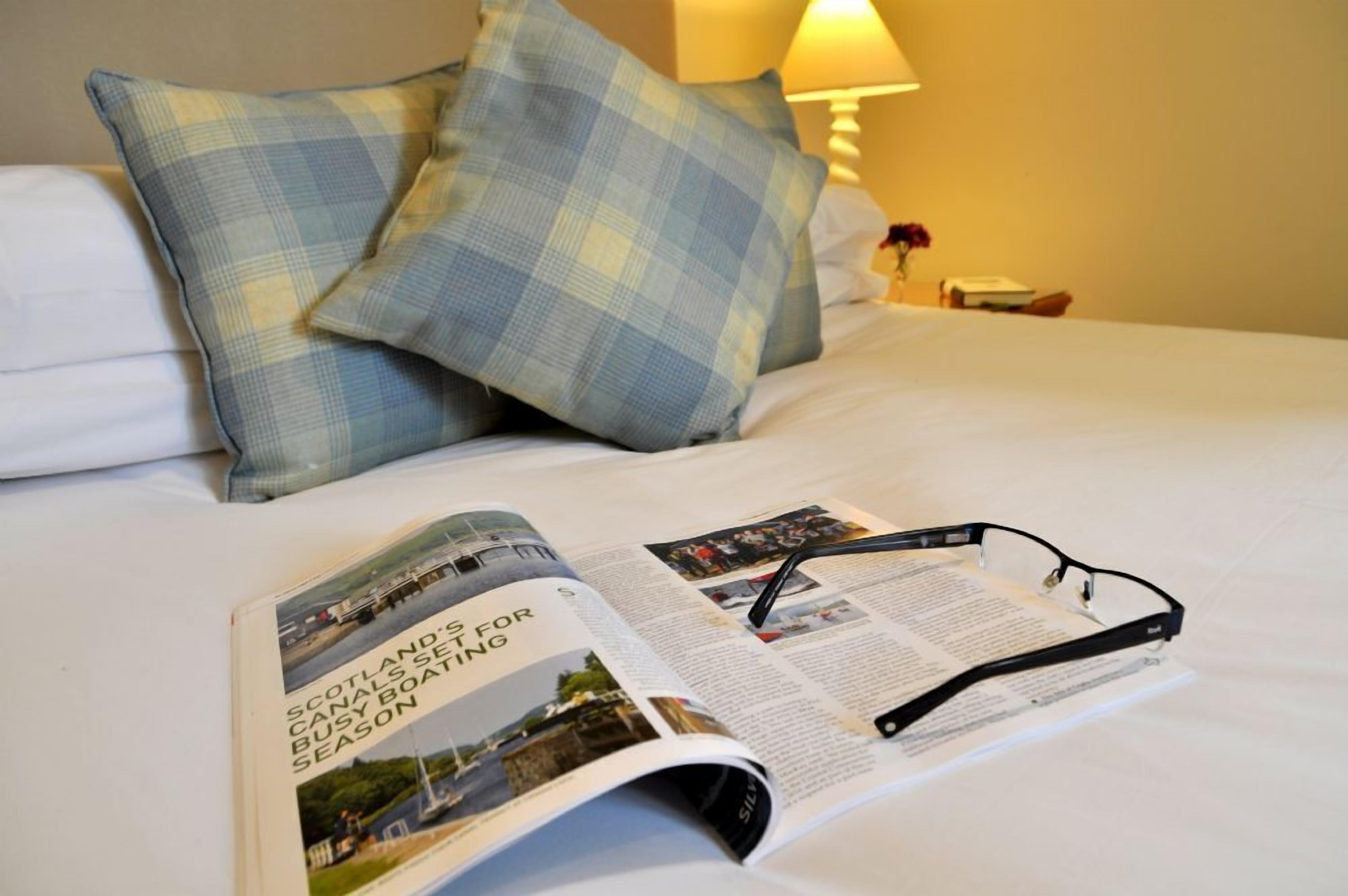Habitació d'hotel amb un llit, una revista i unes ulleres al llit.