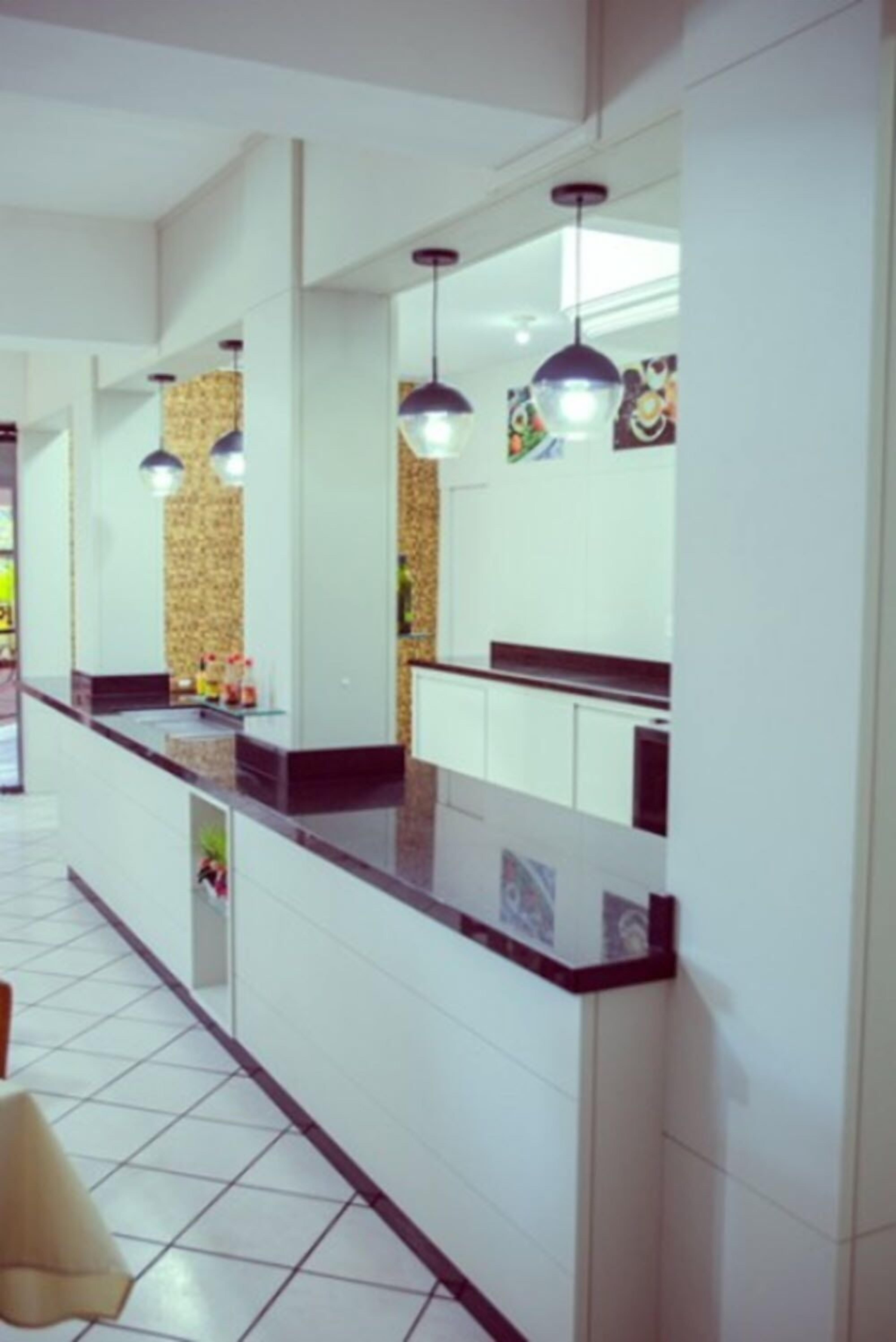 Cozinha moderna com armários brancos, bancada preta e iluminação pendente.