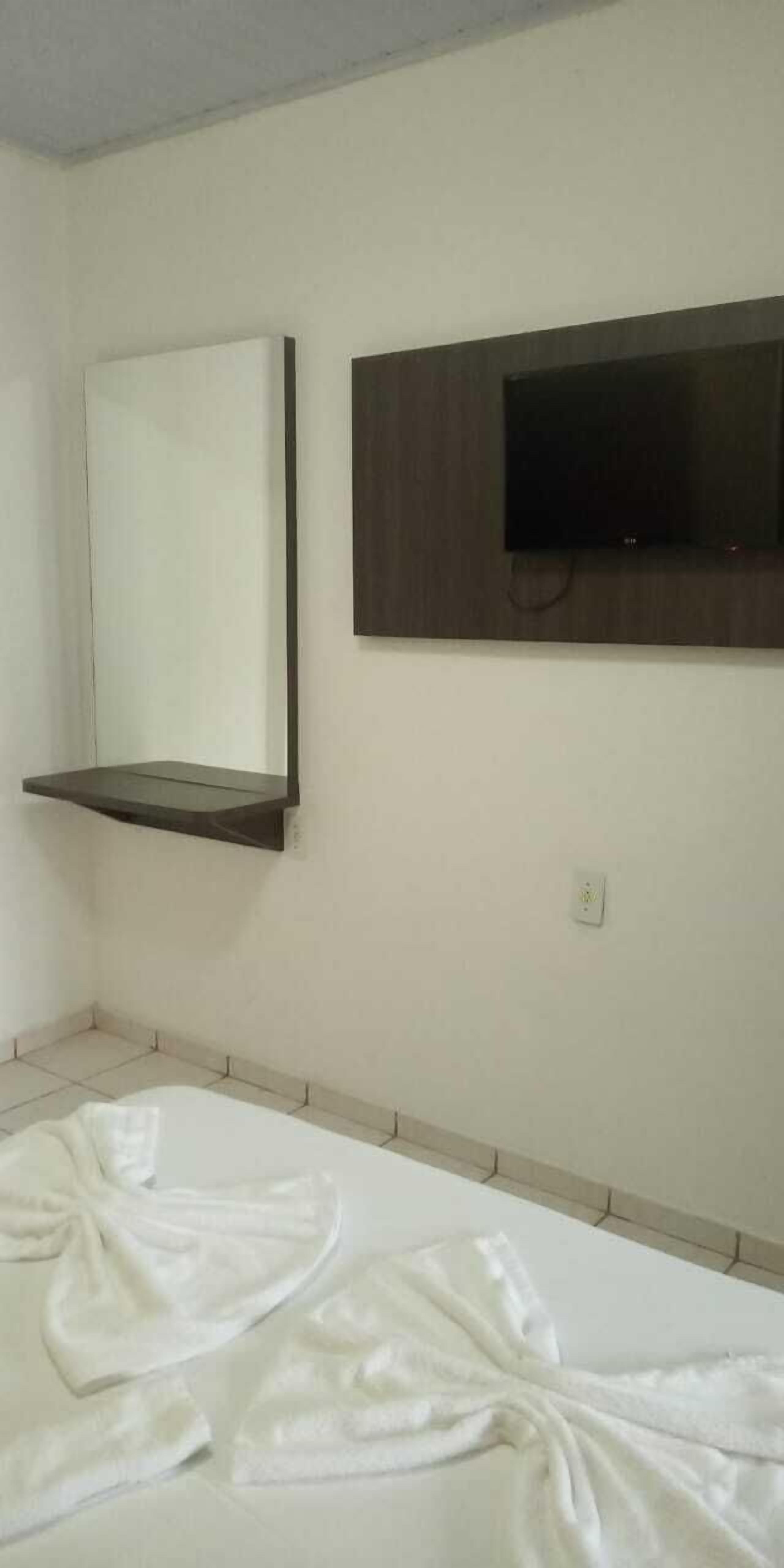 A bedroom with a bed, a wall-mounted TV, and a shelf above the bed.
