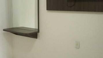 A bedroom with a bed, a wall-mounted TV, and a shelf above the bed.