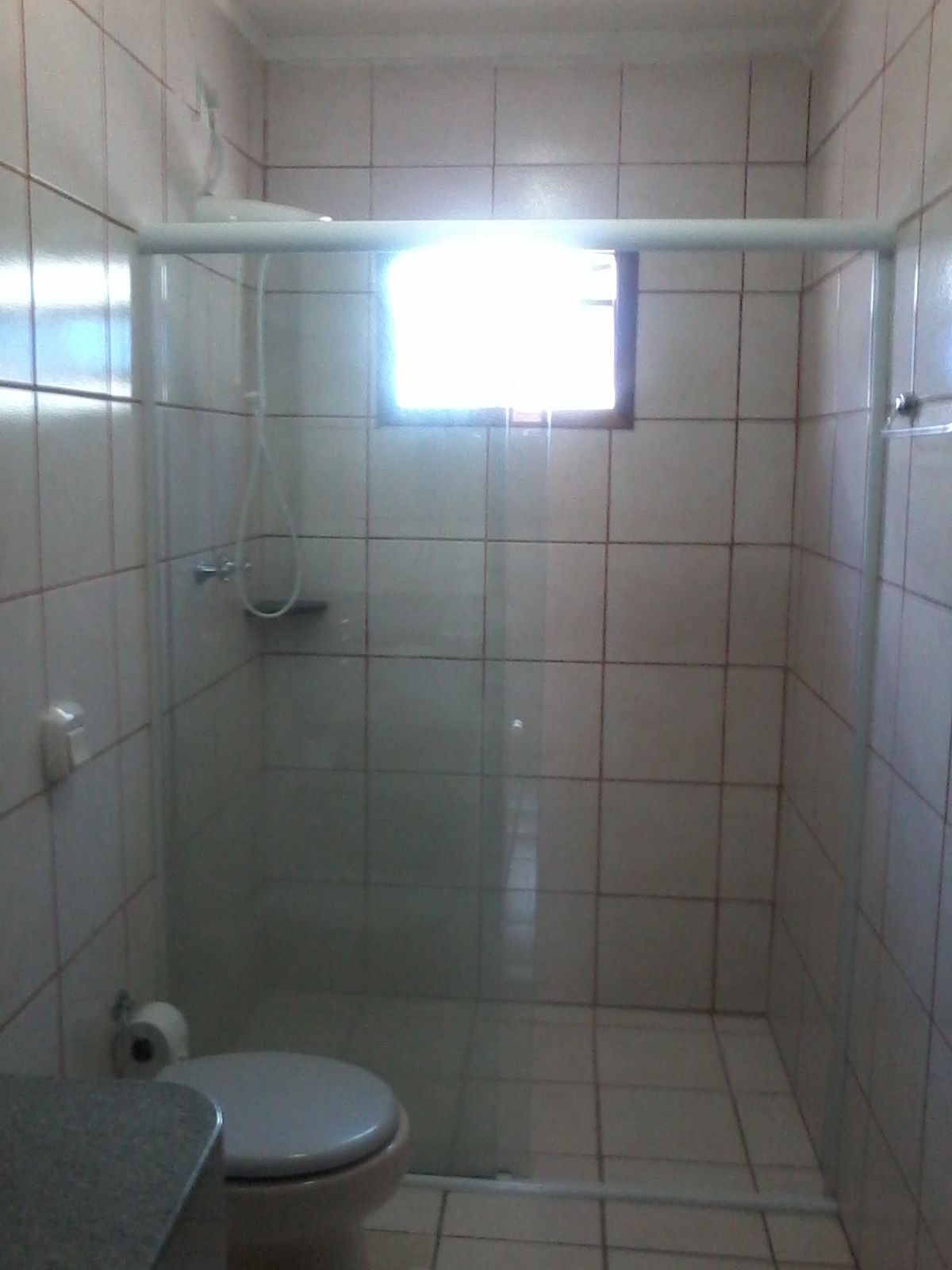 A small, tiled bathroom with a shower enclosure, a toilet, and a window.