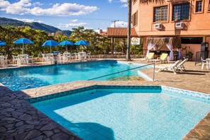A swimming pool with lounge chairs and umbrellas, surrounded by a stone patio and a building with a tiled roof.