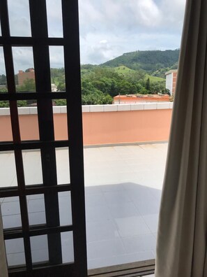 A view from a window with a metal grid, overlooking a rooftop with a tiled floor and a building with a red roof. - Termas Park Hotel (Gravatal)