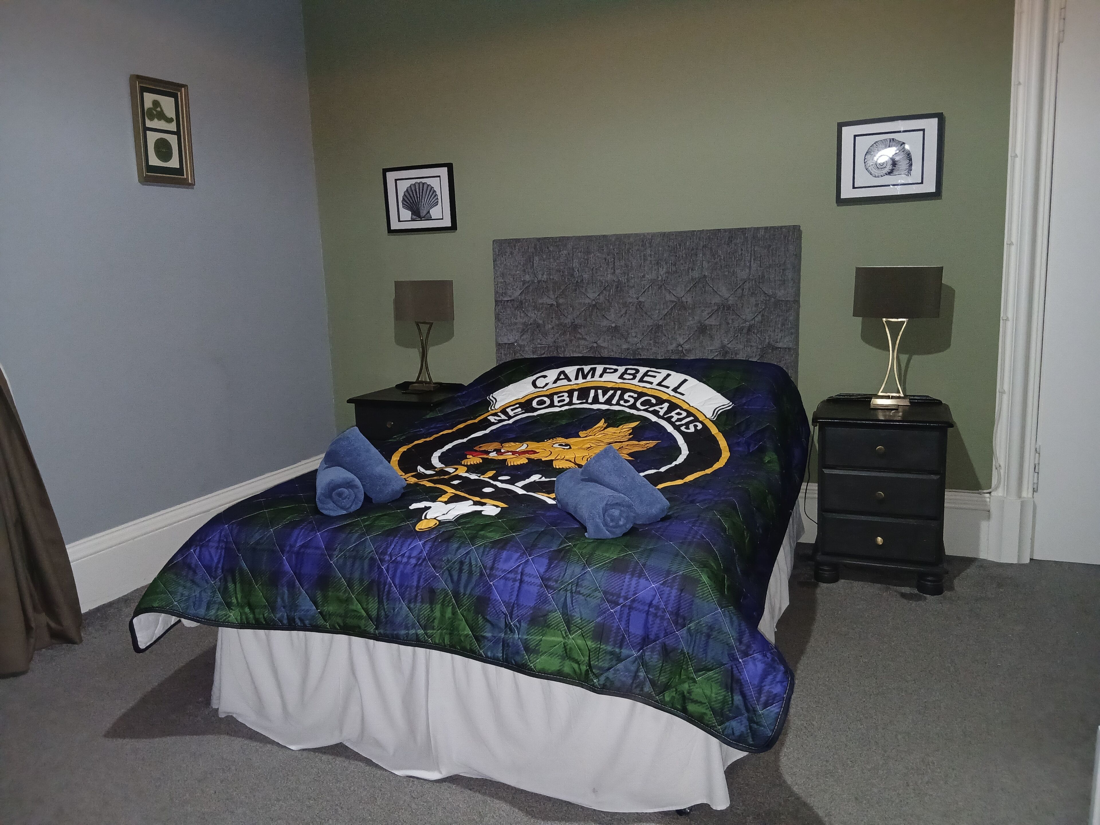 A bedroom with a bed, a nightstand, a lamp, and framed pictures on the wall.