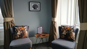 Two chairs with floral cushions, a small round table with a red folder, and framed artwork on the wall. - Greenland House B&B (Castletown)