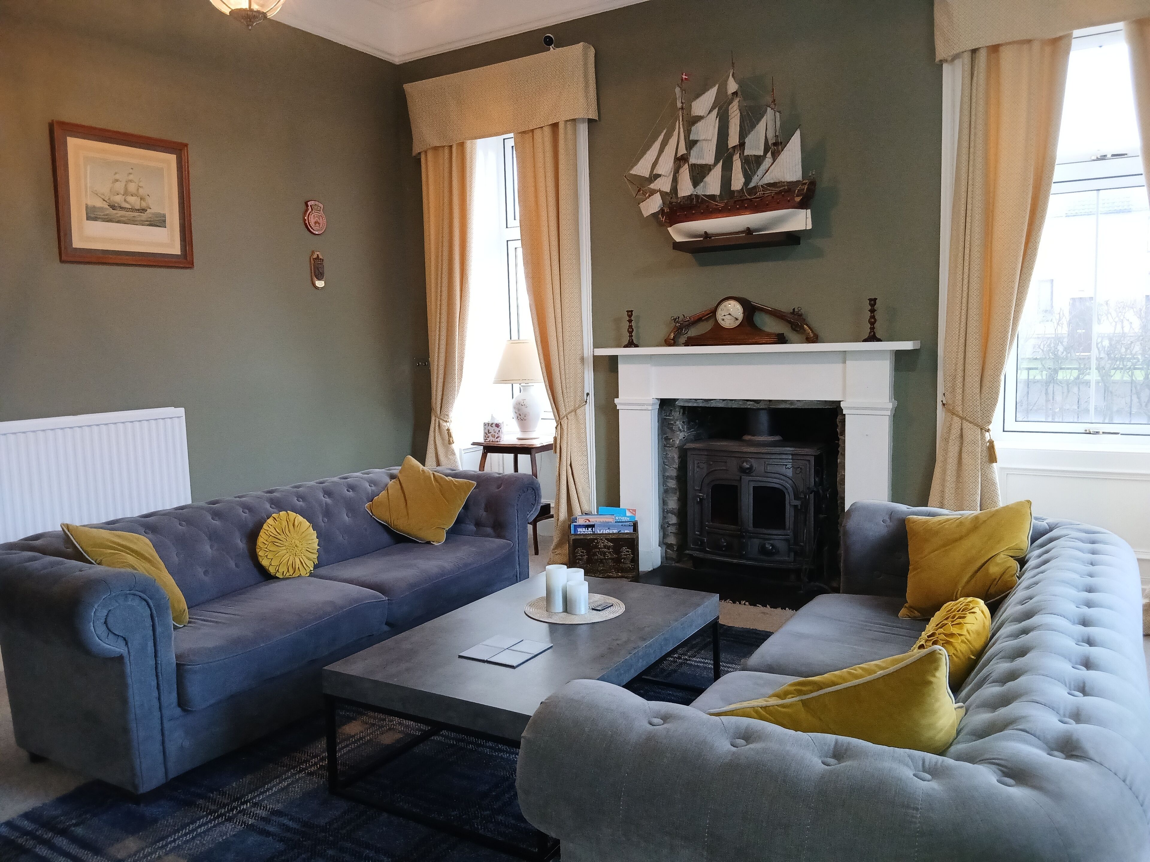 A living room with a blue sofa, a grey sofa, a fireplace, and a ship decoration on the wall.