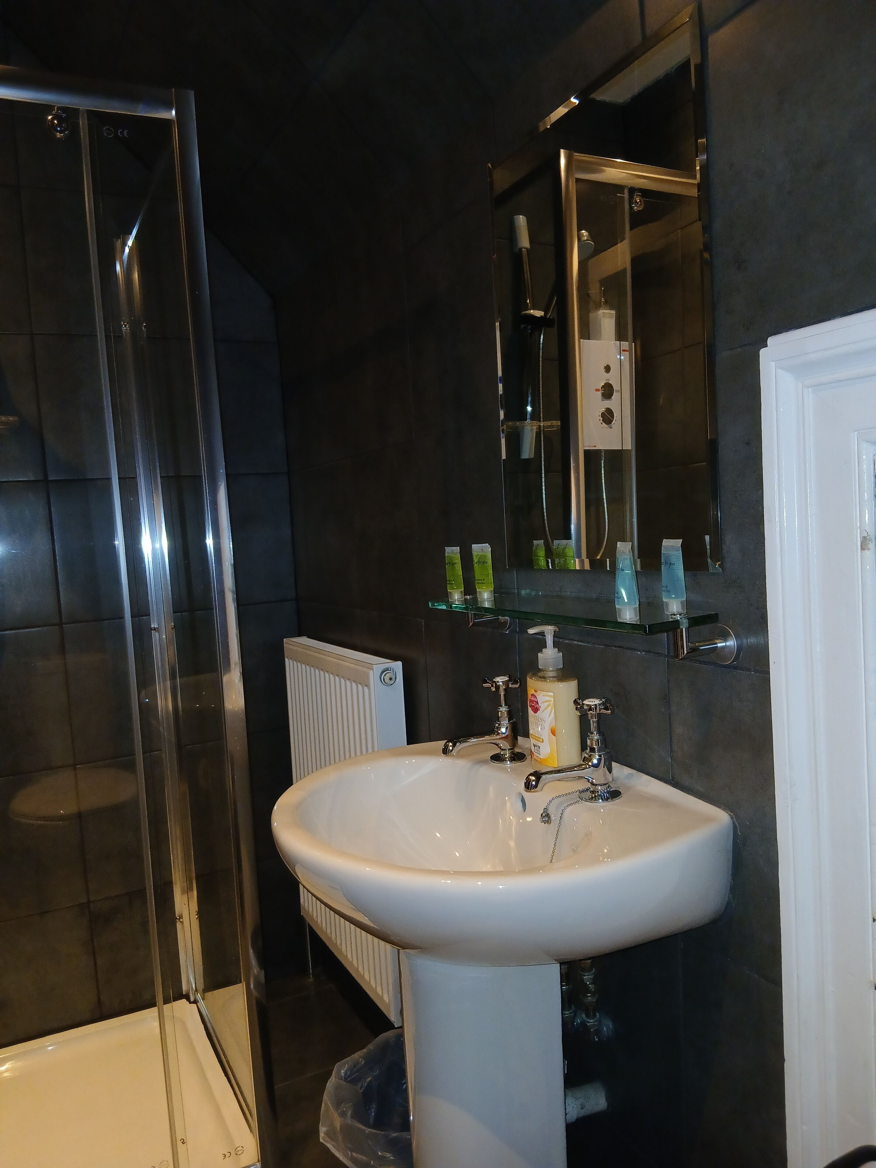 Un baño con cabina de ducha de vidrio, un lavabo blanco con un espejo encima y un radiador blanco.