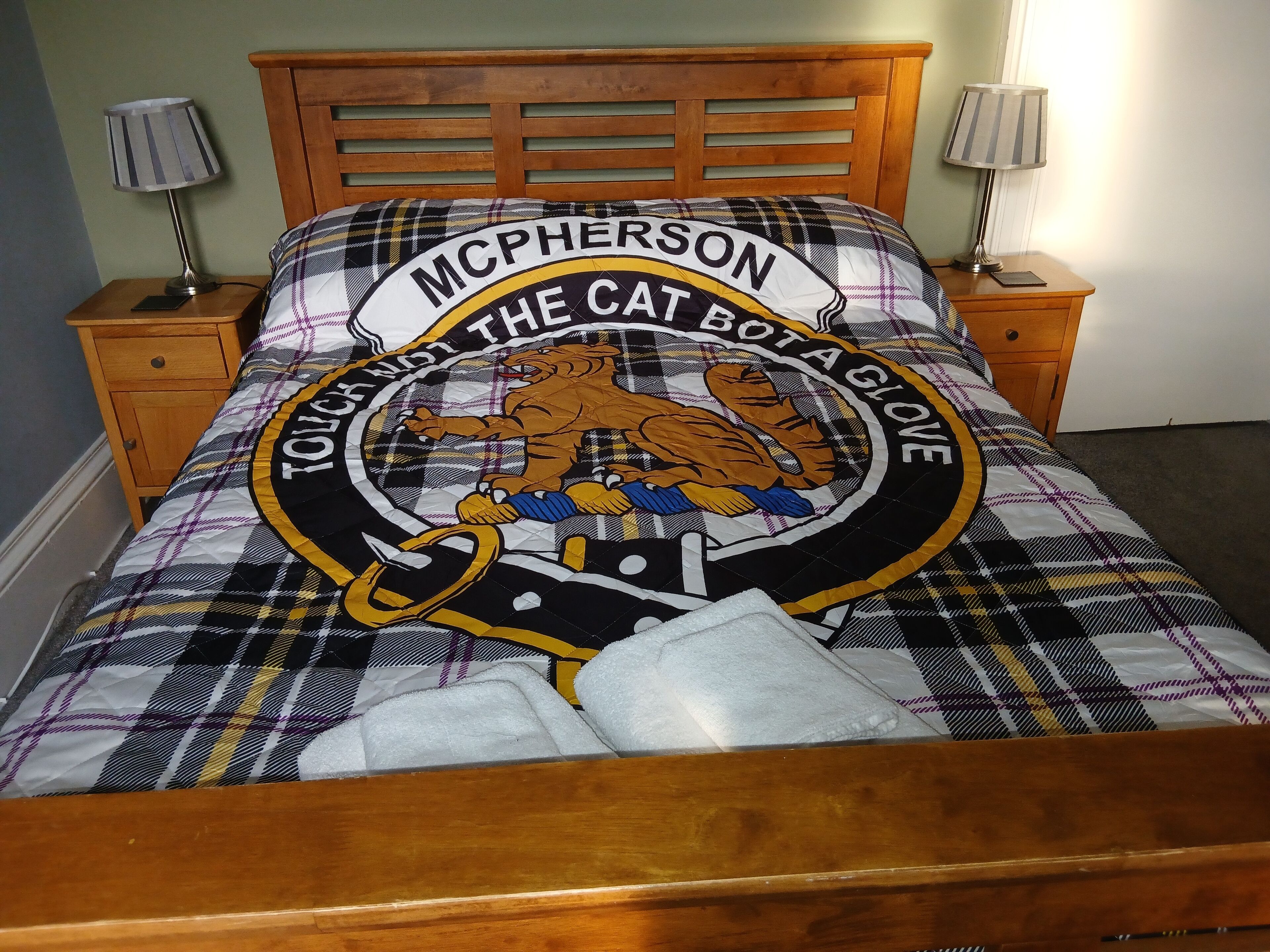 A bed with a plaid blanket featuring a tiger and the text "McPherson The Cat Bot a Cowe."