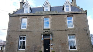 A two-story stone building with a black front door, multiple windows, and a sign reading "GREENLAND HOUSE". - Greenland House B&B (Castletown)