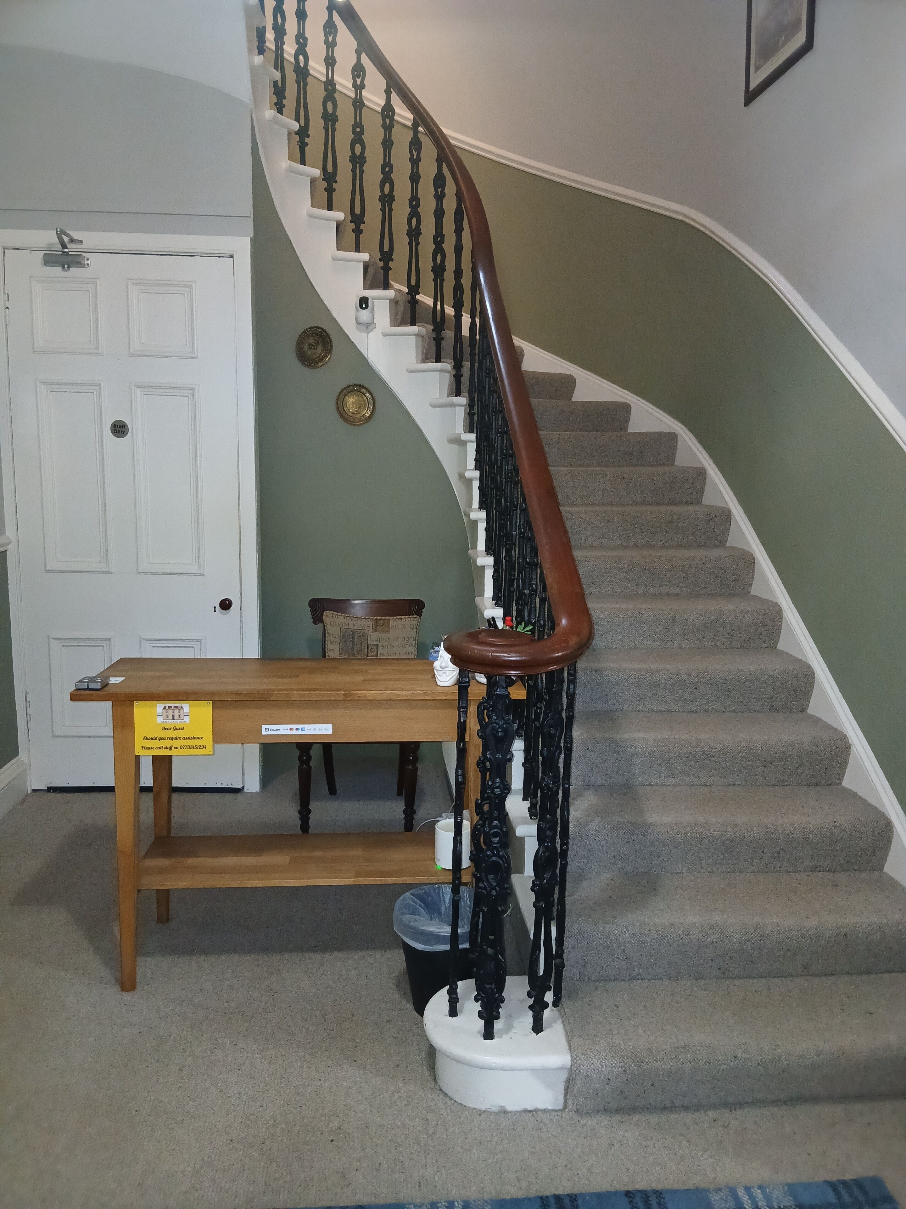 A staircase with a wooden handrail and a white banister, leading to a landing with a bench and a trash can.