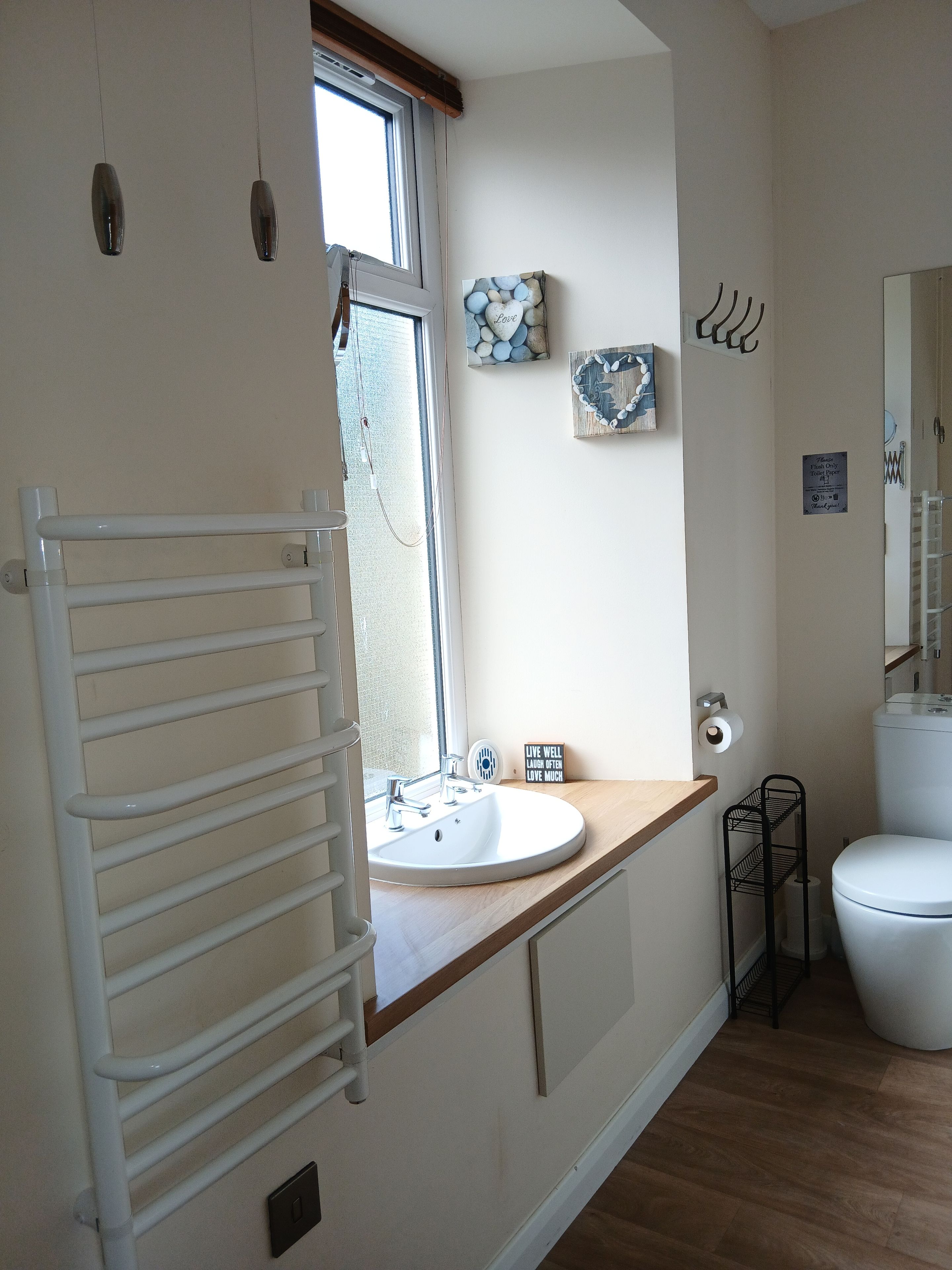 A bathroom with a white sink, a toilet, a towel rack, and a window.
