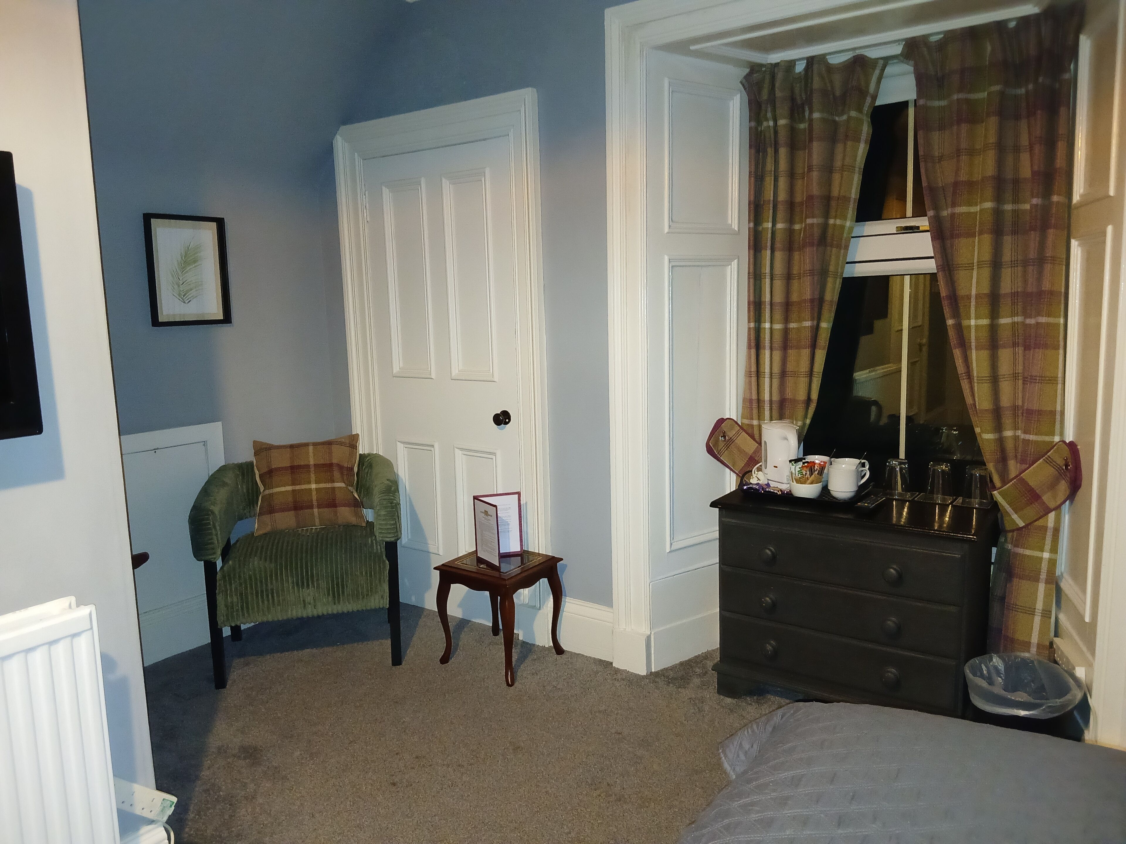 Une chambre à coucher avec un fauteuil vert, une commode, un tableau encadré et une porte.