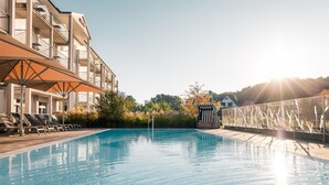 Una piscina con sillones de descanso y sombrillas, rodeada de edificios y follaje.