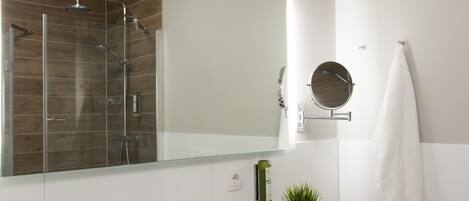 A modern bathroom with a large mirror, a white sink, a shower, and a towel hanging on the wall.