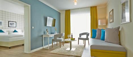 A modern hotel room with a bed, a desk, a sofa, and a dining area.