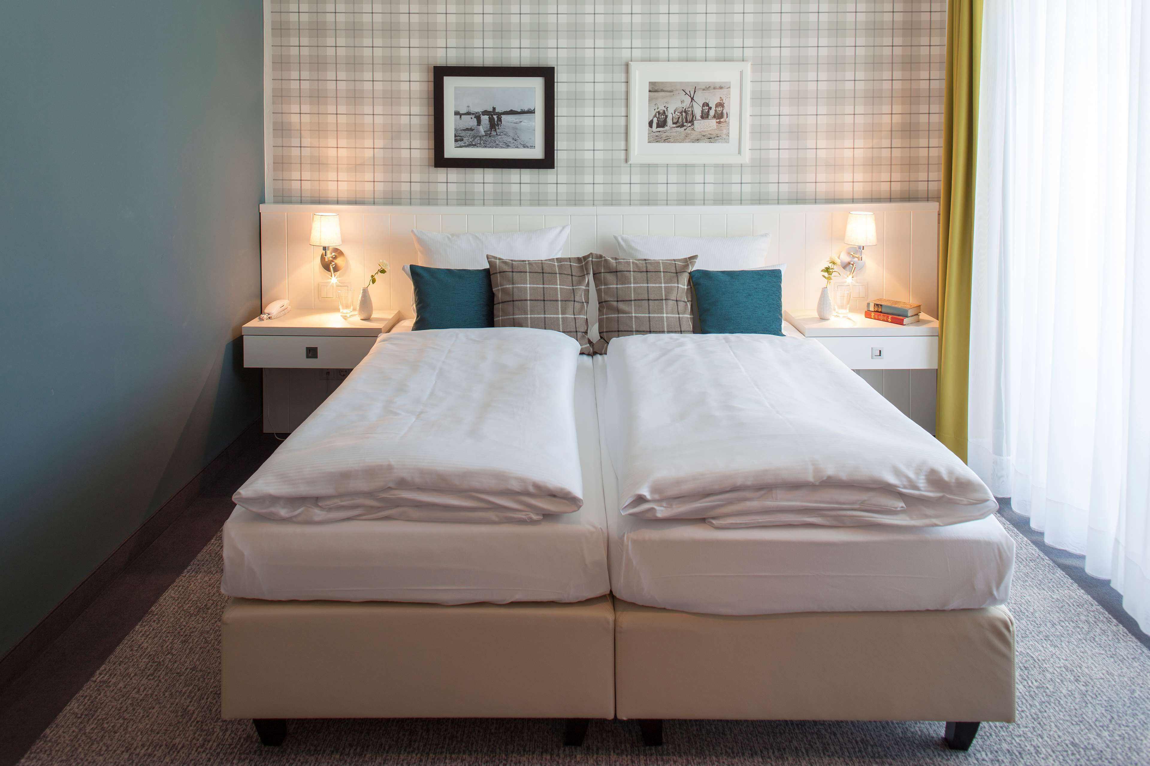 A double bed with white linens, two bedside tables with lamps, and a checkered pillow.