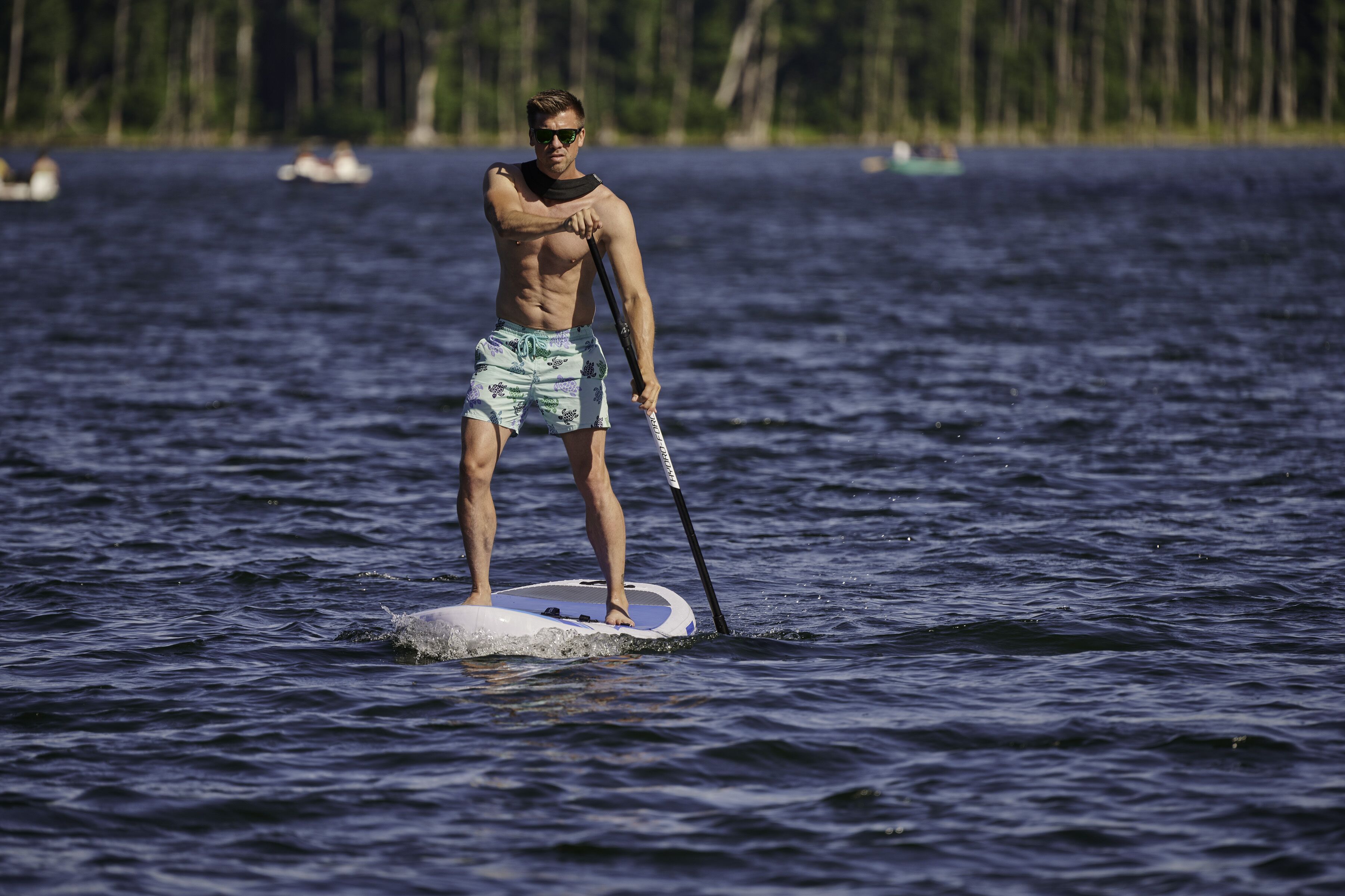 A person paddleboarding on a calm body of water with trees in the background.
