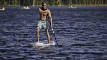 Una persona haciendo paddleboard en aguas tranquilas, con árboles al fondo.