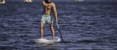 A person paddleboarding on a calm body of water with trees in the background.