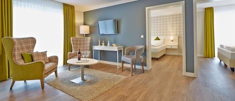 Un salon moderne avec un canapé, un fauteuil, une table basse et un téléviseur fixé au mur.