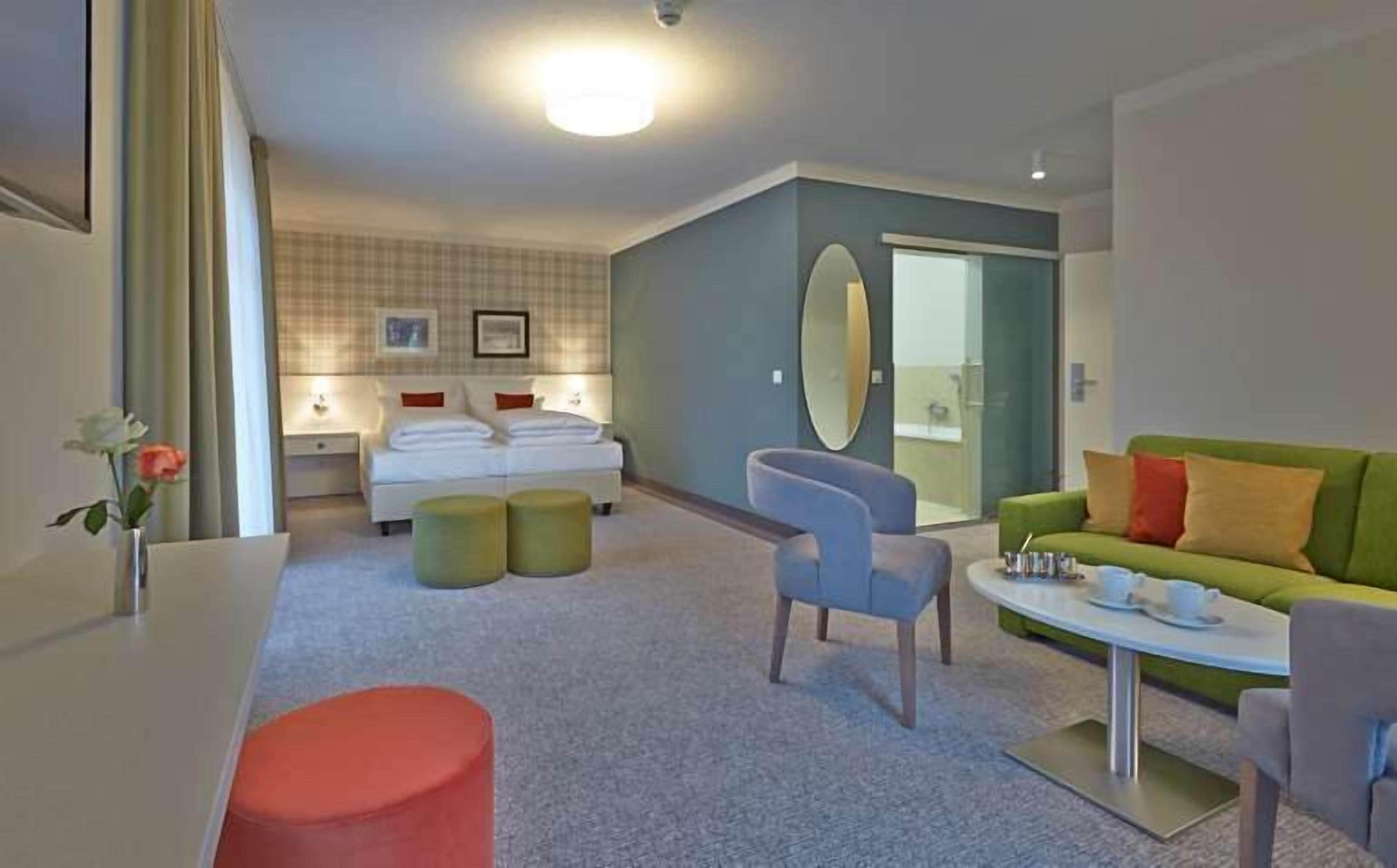A modern hotel room with a bed, a green sofa, a small table, and a chair.
