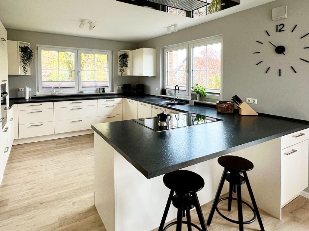 A modern kitchen with a large island, white cabinetry, and a black countertop. There are two black bar stools at the island.