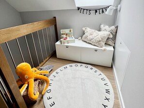 A child's play area with a wooden crib, a white play table, and alphabet-themed rugs.
