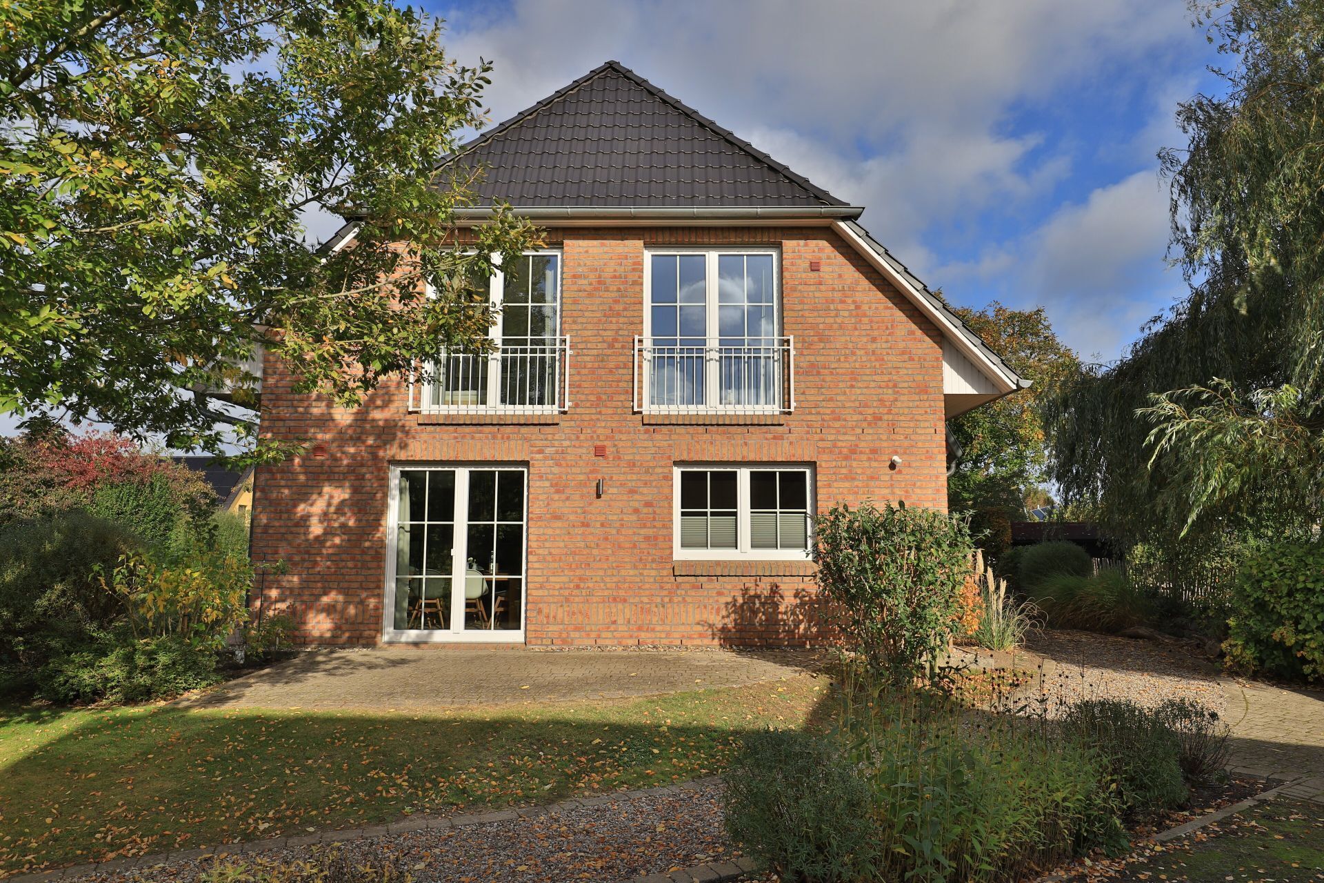 Een tweelaags bakstenen huis met een veranda, grote ramen en een tuin.