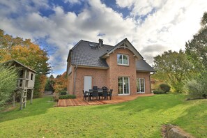 A two-story house with a brick exterior, a tiled roof, and a front porch with a table and chairs.