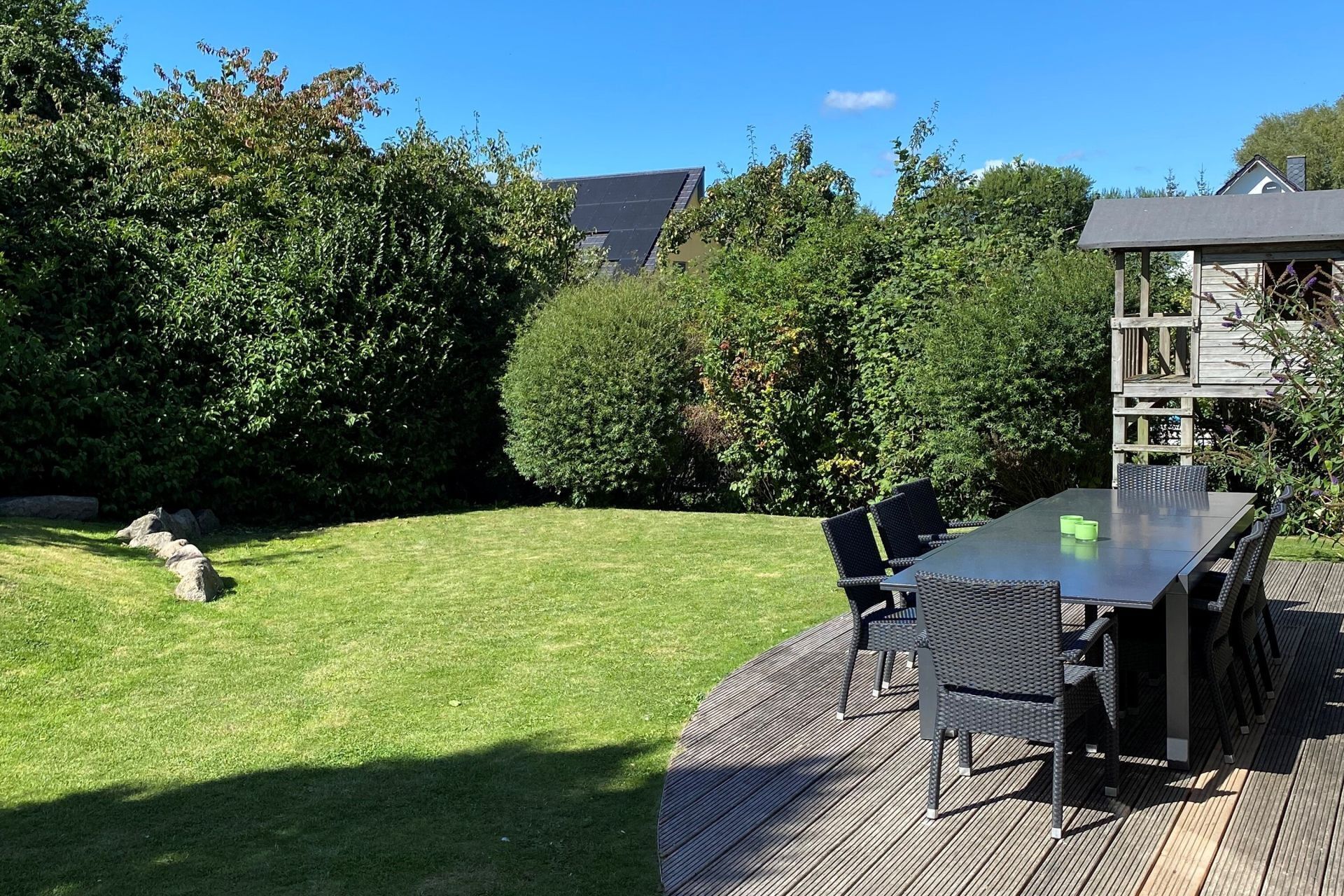 Eine Terrasse mit Tisch und Stühlen, umgeben von einem gepflegten Rasen und üppiger Bepflanzung.