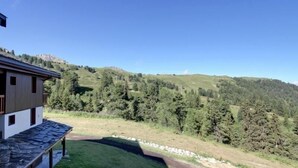 A modern building with a stone roof, surrounded by a lush green landscape and a mountain in the background.