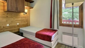 A room with two beds, wooden paneling, a window with curtains, and a radiator.