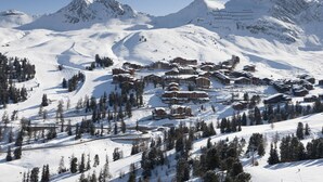 A snow-covered mountain resort with multiple chalet-style buildings, ski slopes, and a clear sky.