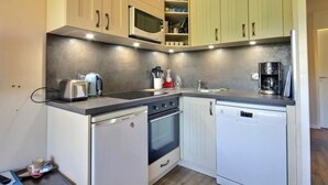 A compact kitchen with white and green cabinets, a microwave, a coffee maker, and a dishwasher.