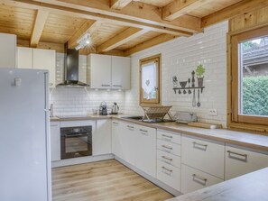 Una cocina moderna con armarios blancos, techo de madera y ventana con vistas a zonas verdes.
