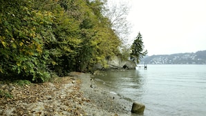 Une plage bordée d’un rivage rocheux, une jetée s’avançant dans une eau calme et une végétation dense sur la gauche.