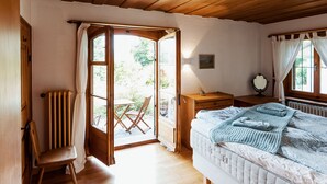 Une chambre confortable avec un plafond en bois, un lit recouvert d’une couverture bleue, une chaise en bois et une vue sur l’extérieur par une porte ouverte.