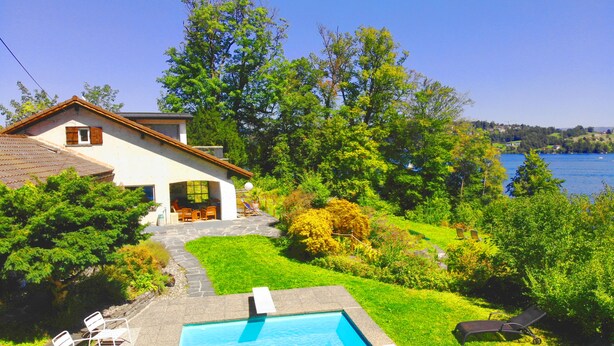Une piscine avec des chaises longues, une maison dotée d’un jardin et une vue sur un lac.