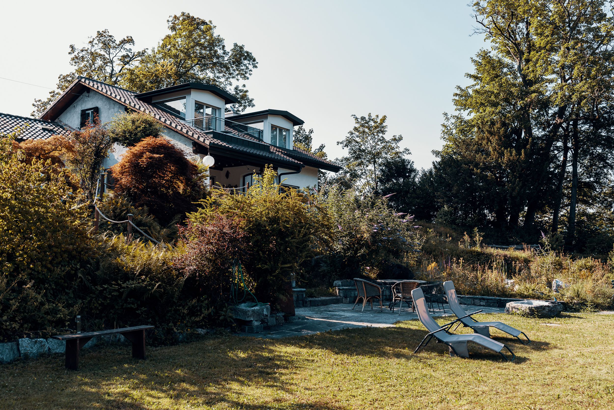 A house with a garden, a bench, and two lounge chairs.